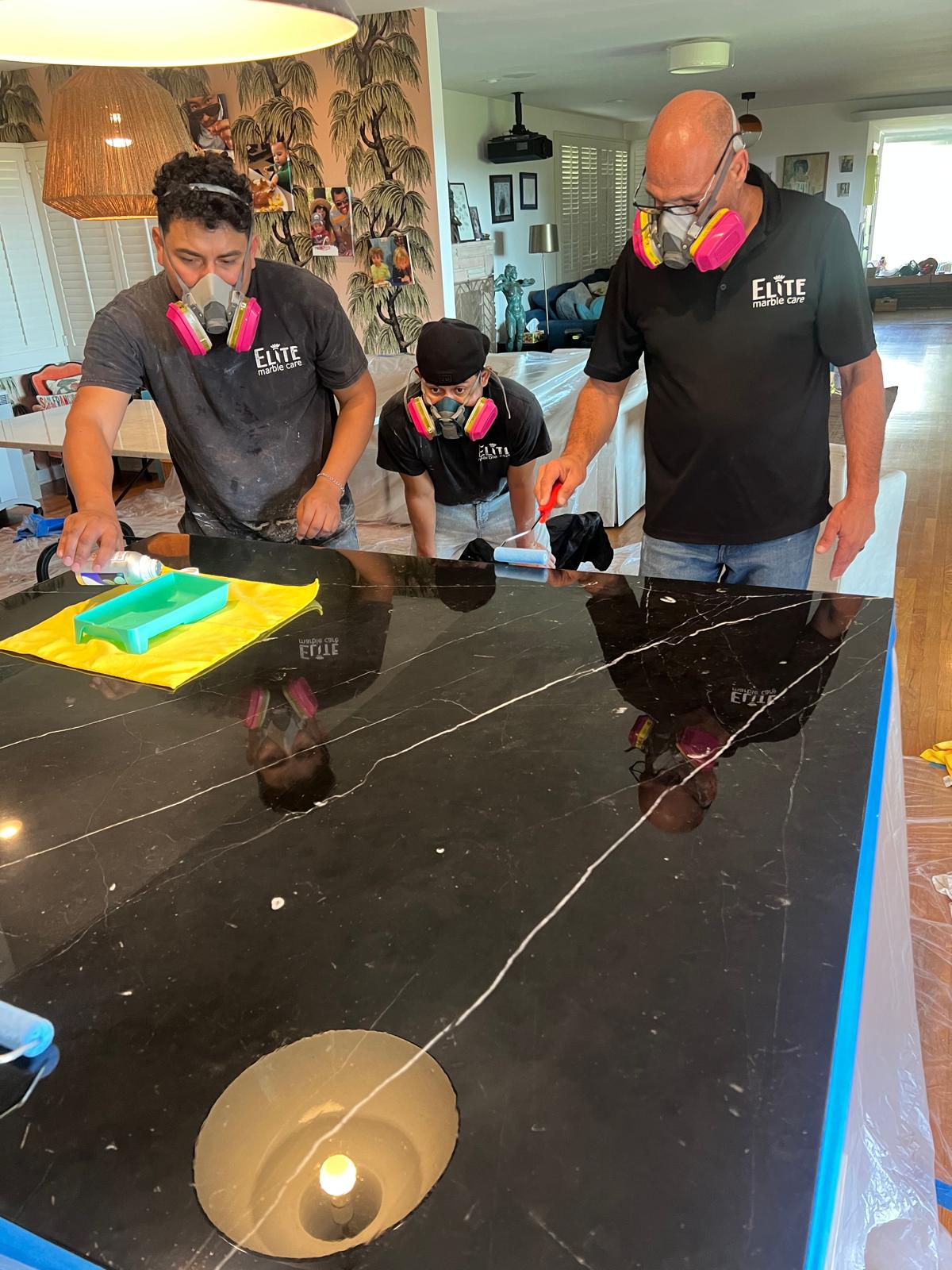 Technician applying protective sealant to a black marble countertop