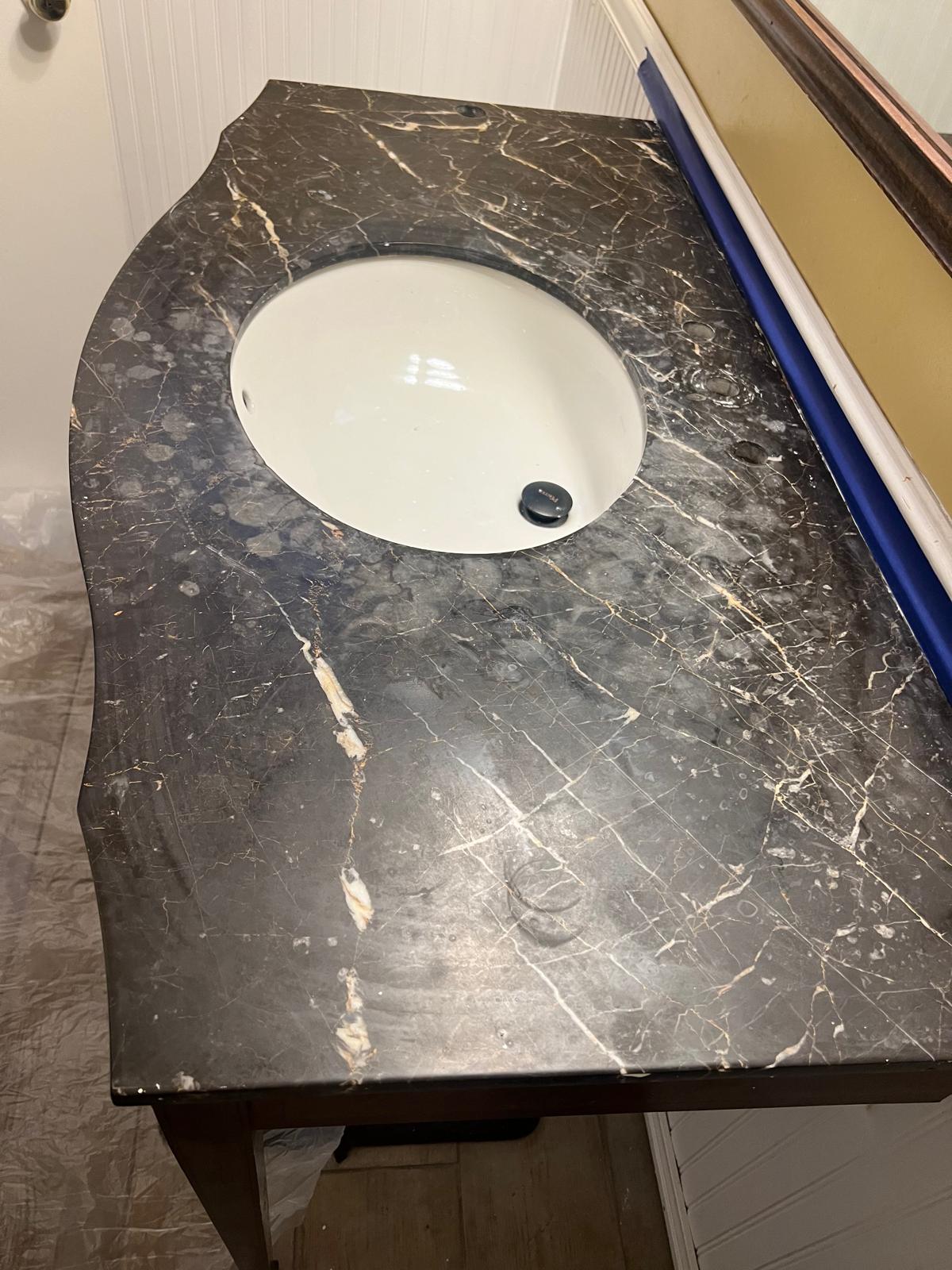 Dark marble vanity showing dull etched areas around the sink