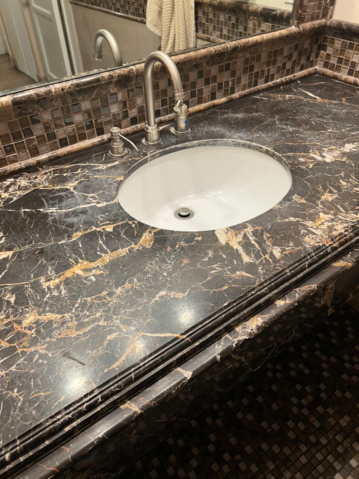 Dark marble countertop with light etch marks around the sink