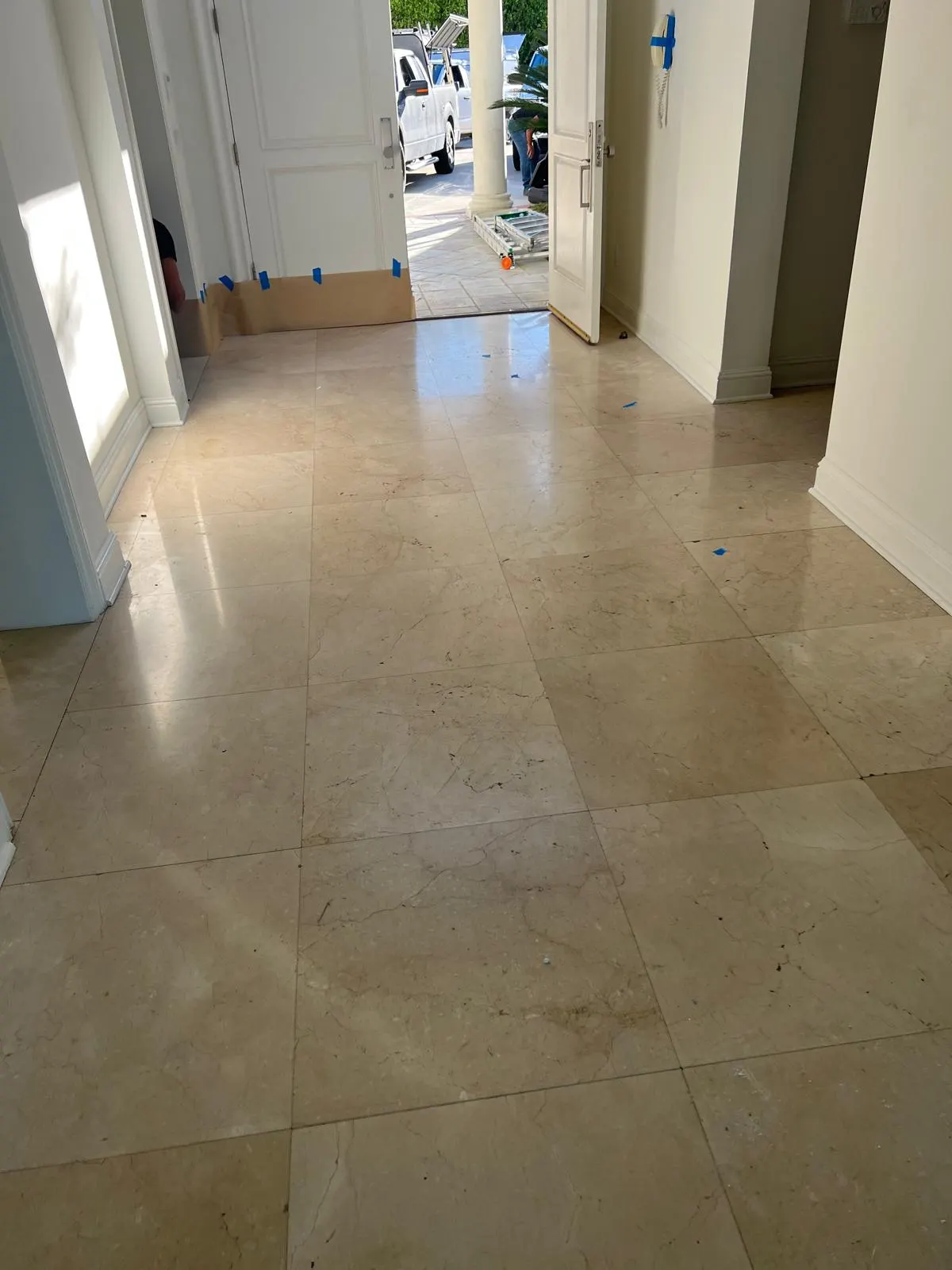 Light natural stone entry floor beside a doorway with renovation masking and protective board